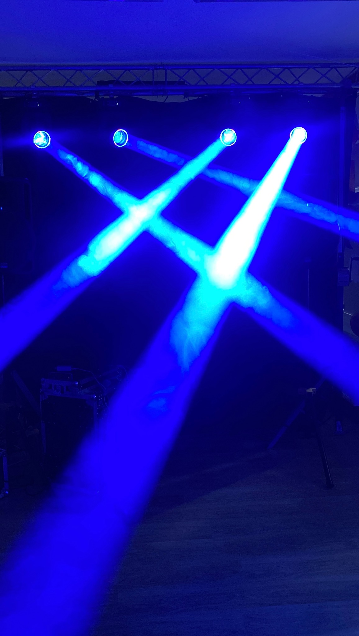 Scena oświetlona niebieskimi reflektorami krzyżującymi się w Węgorzewie. Widoczne elementy konstrukcji scenicznej i podłoga.