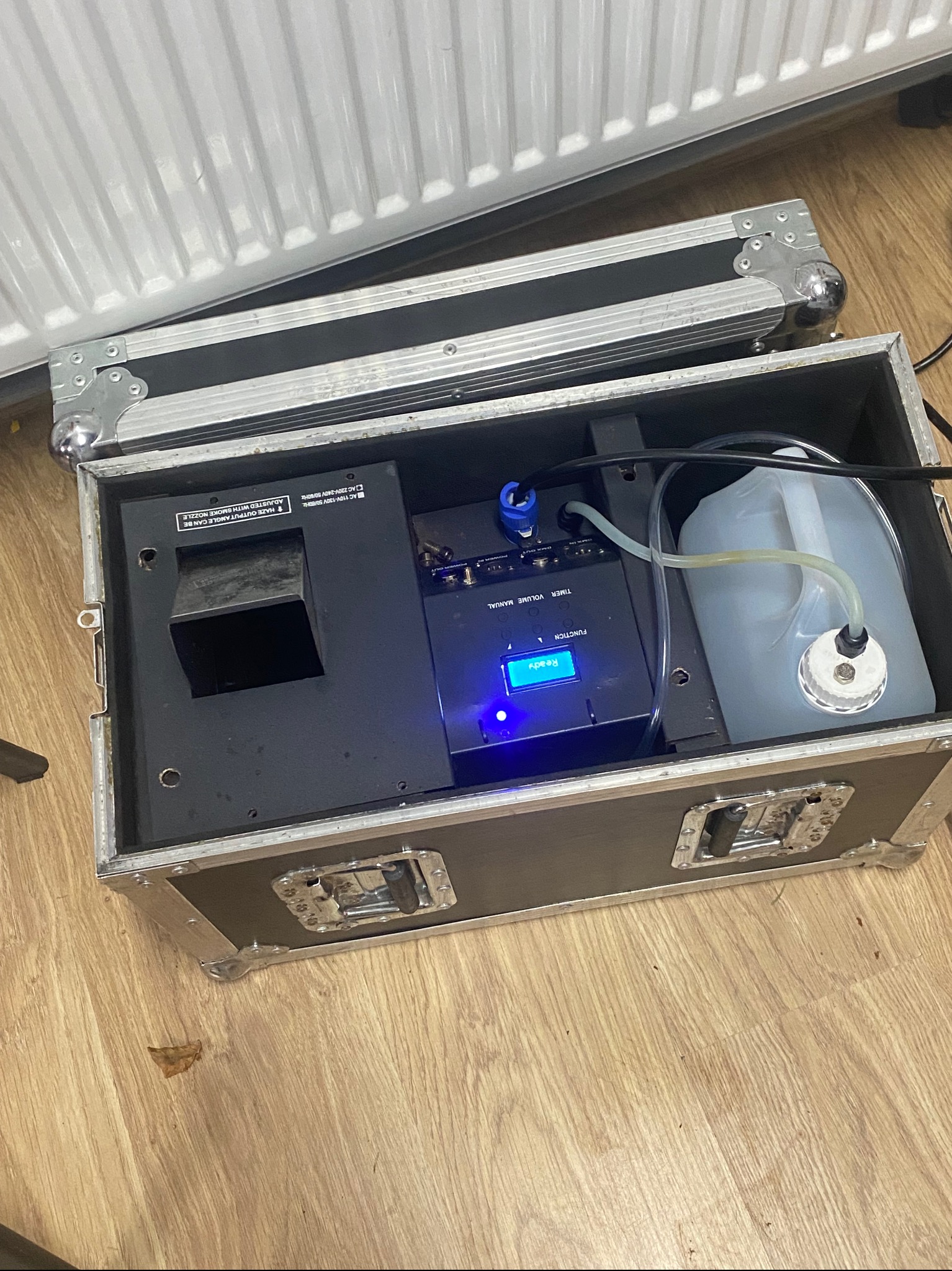 Maszyna do dymu w skrzyni transportowej, widoczny zbiornik na płyn i panel sterowania z podświetlanym ekranem. Sprzęt eventowy dla zespołu muzycznego.