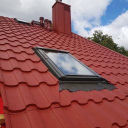 Jakub Wiencko - Czerwony dach z blachodachówki modułowej w Krypno Kościelne, z oknem dachowym i kominem w tym samym kolorze, na tle błękitnego nieba z chmurami.