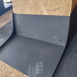 Jakub Wiencko - Szara, metalowa obróbka blacharska przymocowana śrubami do drewnianej płyty OSB, widoczne ślady po montażu.