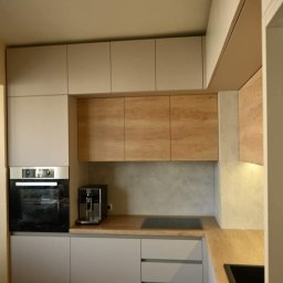 REMONTY I WYKOŃCZENIA PROFESIONALNIE-MATBUDPROFESIONAL MATEUSZ SIKORA - Nowoczesna kuchnia z szarymi szafkami, drewnianymi blatami i sprzętem AGD, z surową żarówką wiszącą na kablu.