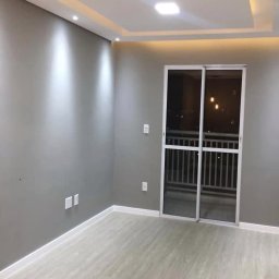 REMONTY I WYKOŃCZENIA PROFESIONALNIE-MATBUDPROFESIONAL MATEUSZ SIKORA - Wnętrze pokoju po odświeżeniu: szare ściany, jasna podłoga imitująca drewno, przesuwne drzwi balkonowe z widokiem na nocne miasto. Sufit podwieszany z oświetleniem punktowym i centralnym.