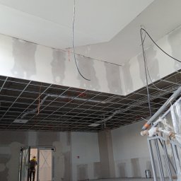 Adrian Korzeniewski - Sufit podwieszany z widoczną konstrukcją metalową w trakcie montażu w pomieszczeniu szpitalnym, częściowo wykończone ściany wymagające dalszych prac, widoczne przewody elektryczne.