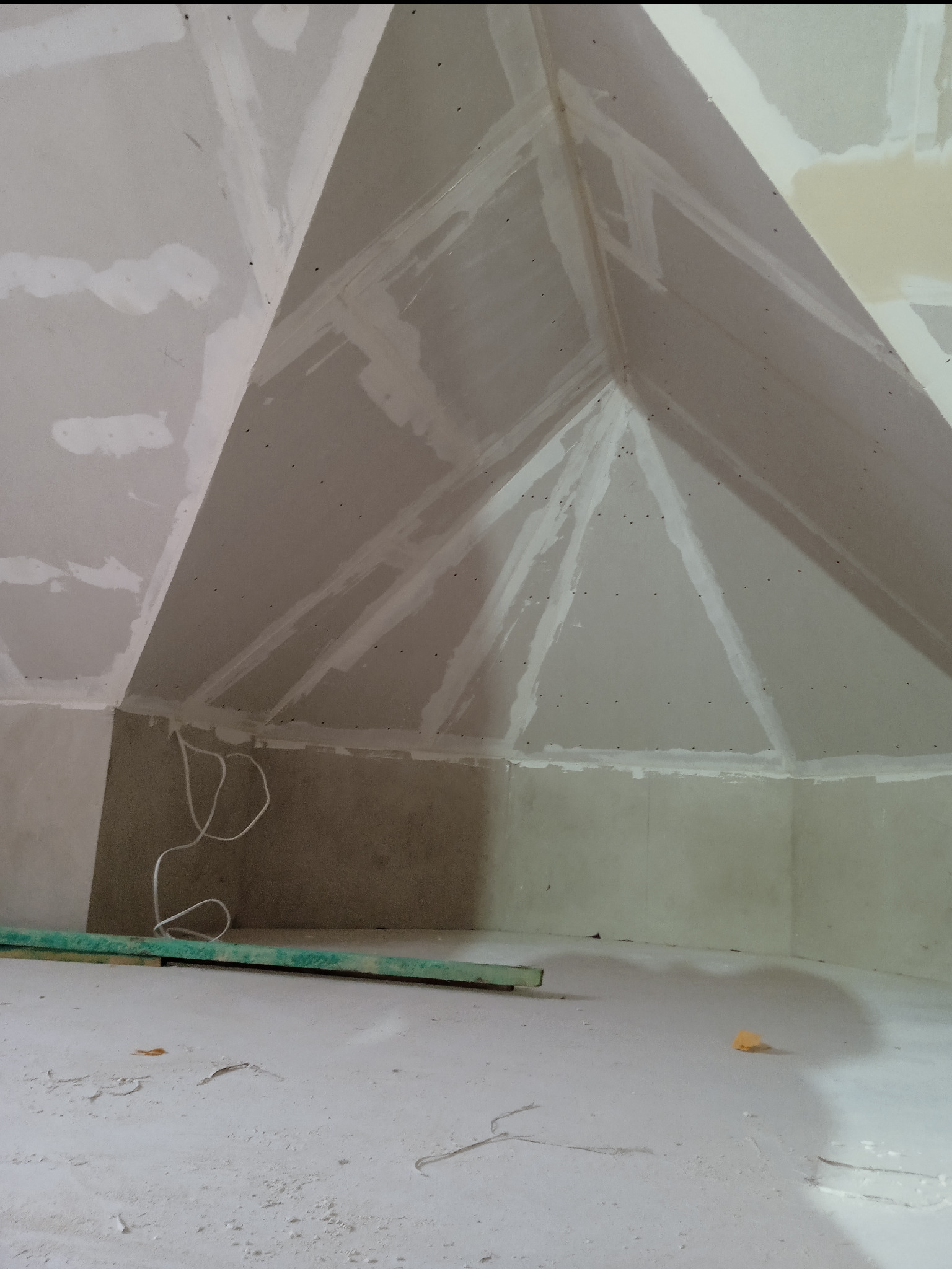 Skośna zabudowa poddasza z płyt karton-gips, widoczne łączenia wzmocnione taśmą i wstępnie zaszpachlowane, przewody elektryczne zwisają ze ściany.