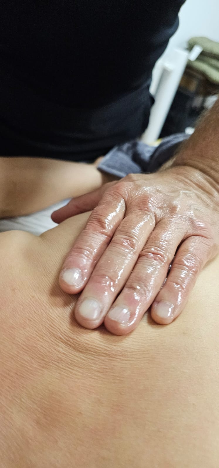 Olejowana dłoń masująca ramię, widoczne zmarszczki na skórze i krótko obcięte paznokcie.