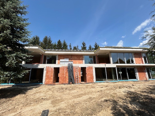 Dwukondygnacyjny budynek w trakcie budowy z czerwonej cegły z dużymi oknami, widoczne rusztowanie i drabina.