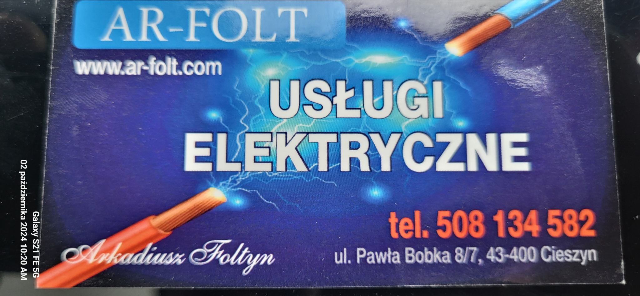 Wizytówka firmy świadczącej usługi elektryczne z numerem telefonu i adresem, z grafiką przewodów i błyskawic na niebieskim tle.