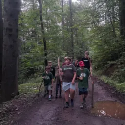 Grupa dzieci z kijkami w lesie, idąca po błotnistej drodze. Uczestnicy leśnej wyprawy edukacyjnej, zorganizowanej przez agencję eventową. Aktywny wypoczynek na łonie natury.