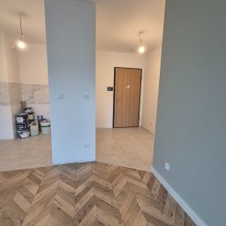 Fedir Melnyk - Ukończone układanie parkietu w jodełkę, widok na świeżo pomalowane ściany i drzwi wejściowe. Częściowo widoczne puszki z farbą.