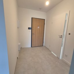 Fedir Melnyk - Jasne wnętrze przedpokoju z drewnianymi drzwiami wejściowymi i białymi drzwiami wewnętrznymi. Szare płytki podłogowe i białe ściany. Minimalistyczny design.