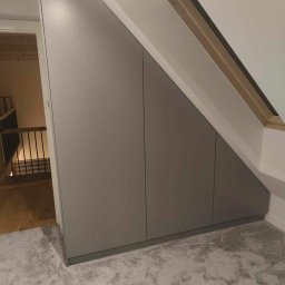 Jakub książek - Szara zabudowa pod skosem na poddaszu z widocznym oknem dachowym i fragmentem schodów z drewnianą balustradą.