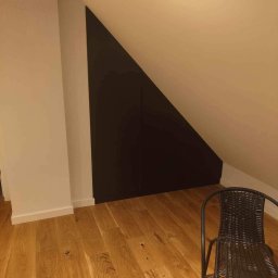 Jakub książek - Ciemna, dwudrzwiowa szafa wnękowa pod skosem dachu, drewniana podłoga, krzesło z rattanu w rogu pokoju.