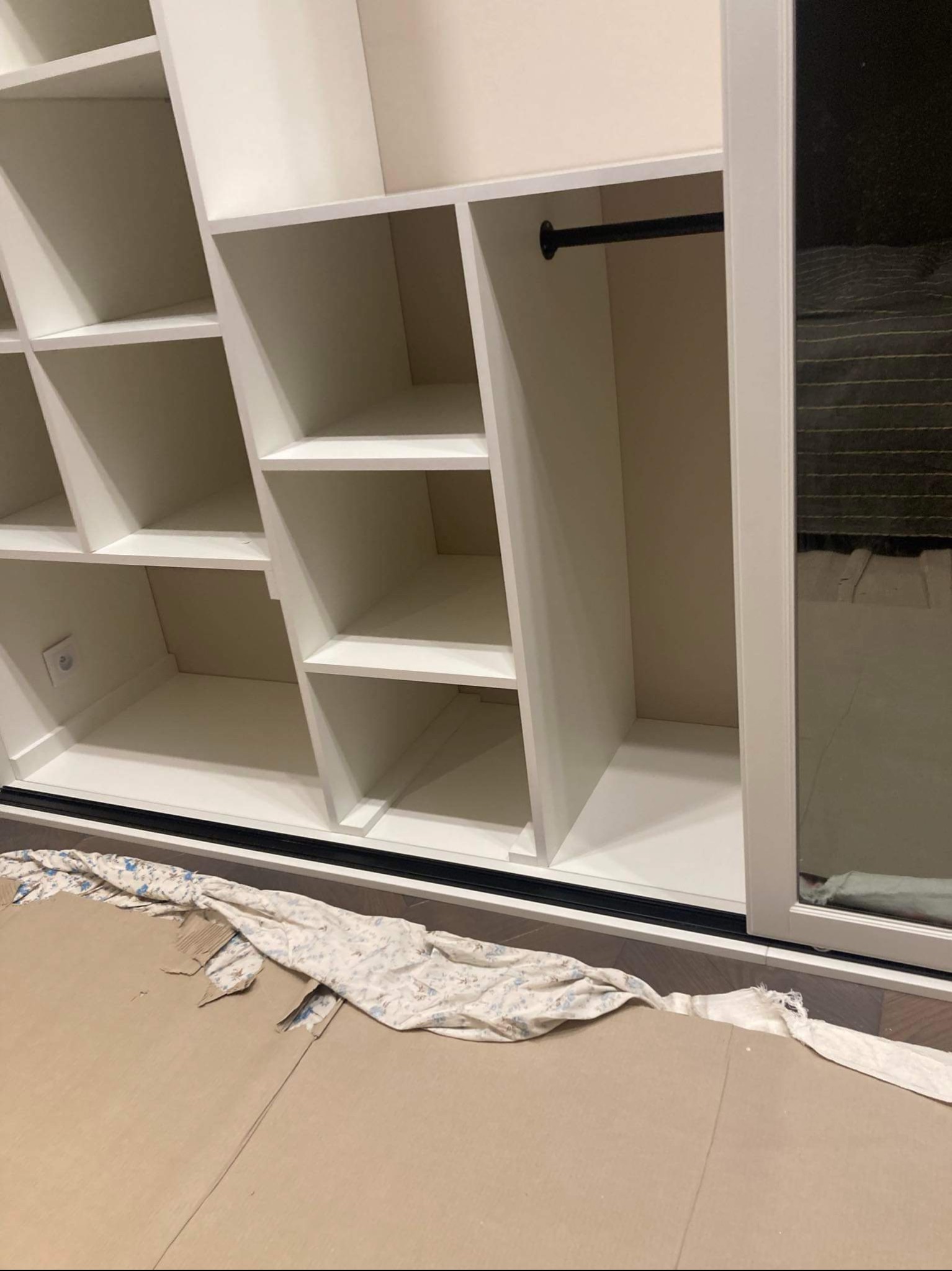 Biała szafa wnękowa z przesuwnymi drzwiami, widoczne półki i drążek na ubrania, zabezpieczona kartonem i tkaniną podczas montażu.