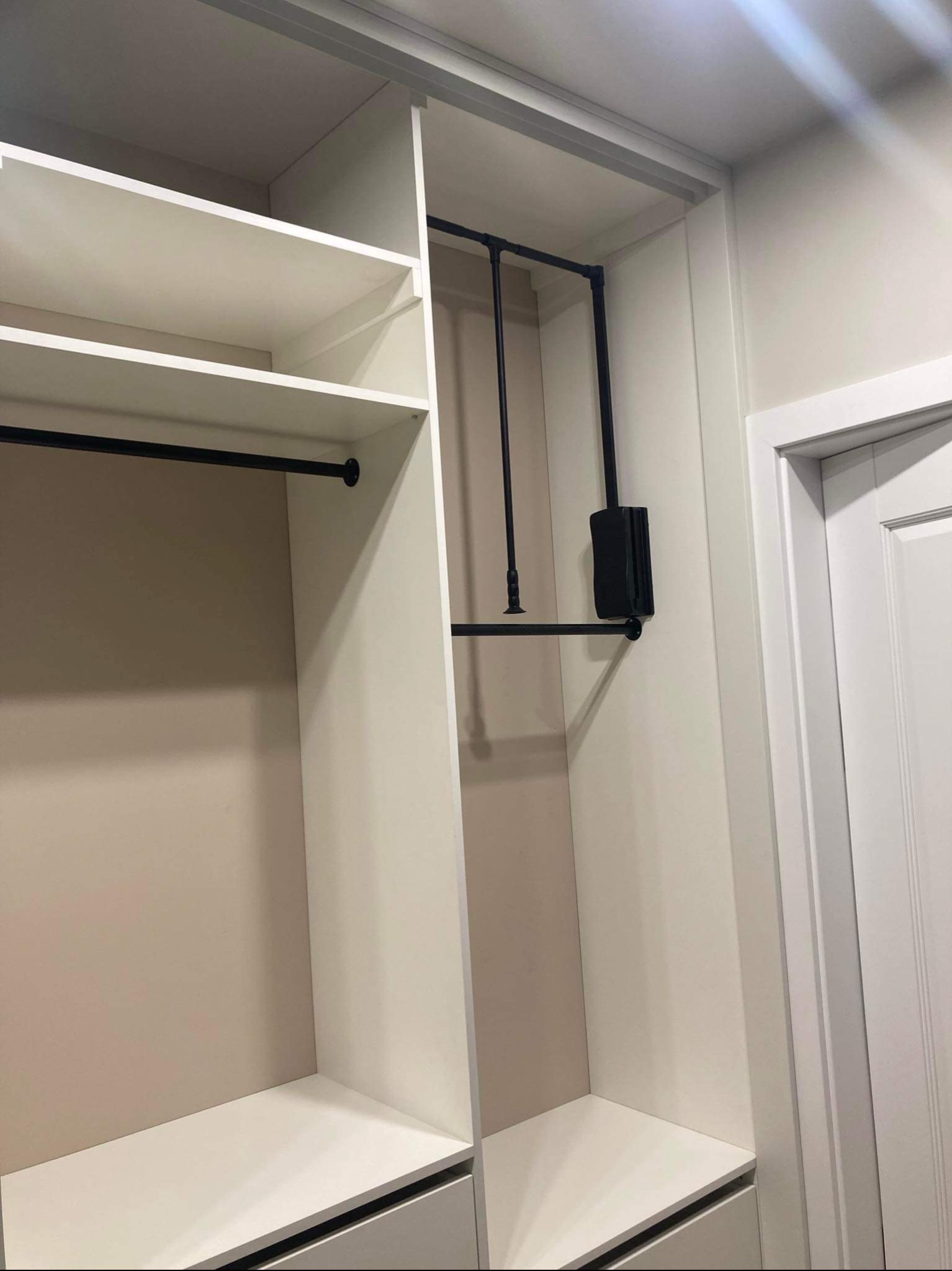 Wnętrze białej szafy wnękowej z czarnymi elementami metalowymi, widoczne półki, drążki i szuflady, minimalistyczny design.