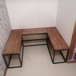 LoftOn - Drewniany blat w kształcie litery U z czarnymi metalowymi nogami, umieszczony w rogu pokoju z tapetą w ptaki i jasnymi ścianami.