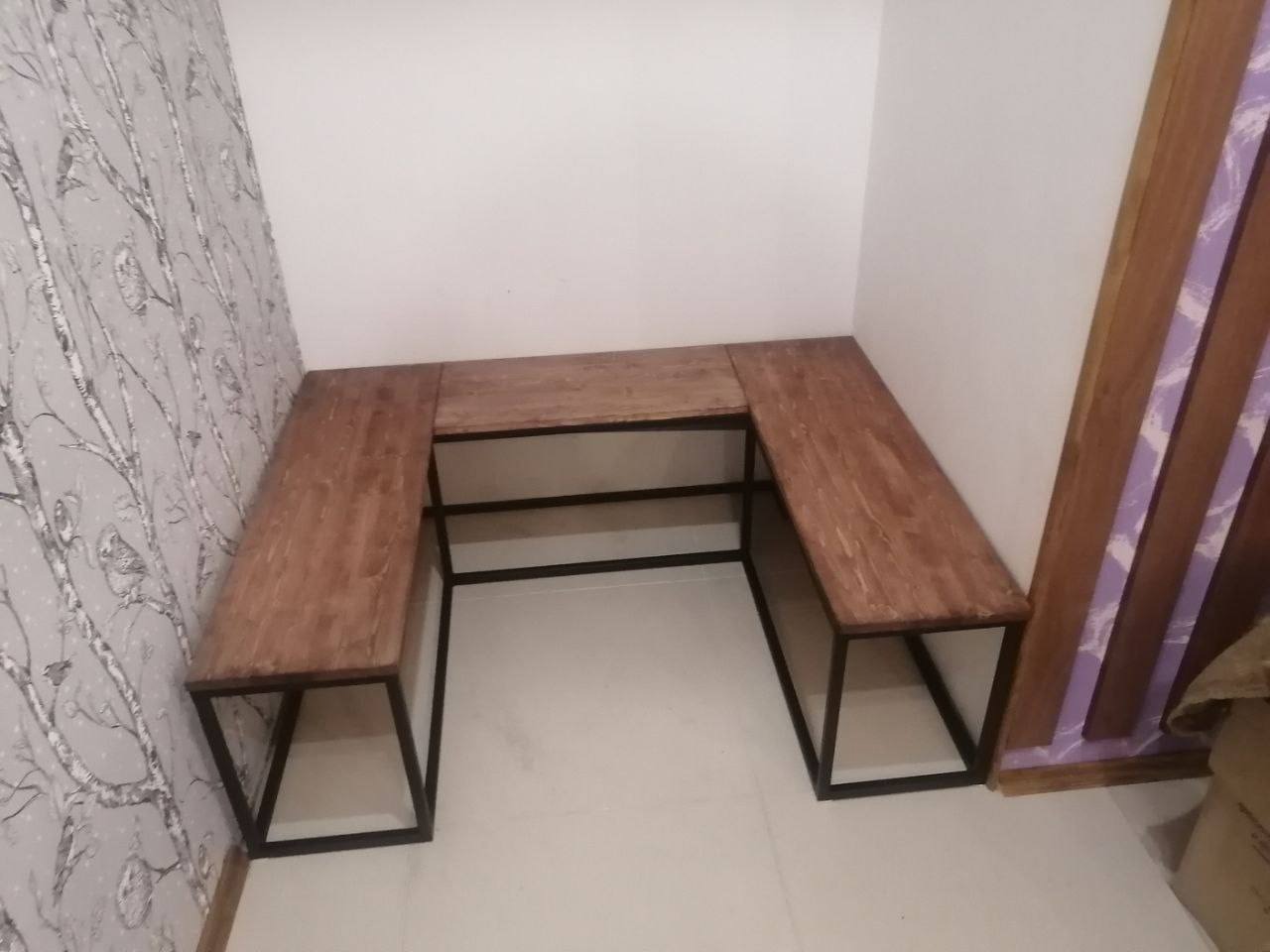 Drewniany blat w kształcie litery U z czarnymi metalowymi nogami, umieszczony w rogu pokoju z tapetą w ptaki i jasnymi ścianami.