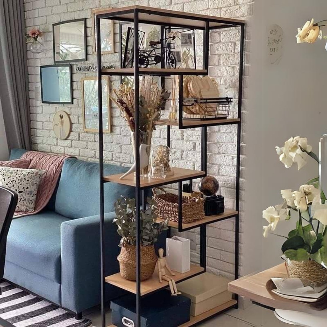 Regał z drewnianymi półkami i czarną metalową ramą, ustawiony w salonie z ceglaną ścianą, udekorowany różnymi przedmiotami dekoracyjnymi, takimi jak wazony z suszonymi kwiatami, koszyki, figurki...