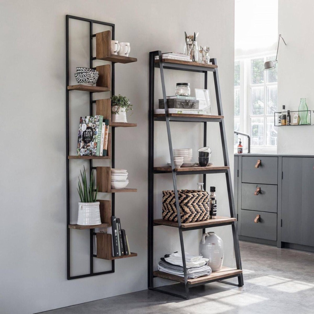 Dwie metalowe półki z drewnianymi blatami w stylu industrialnym, jedna przymocowana do ściany, druga w formie drabiny, eksponujące dekoracje, naczynia i książki w nowoczesnym wnętrzu.