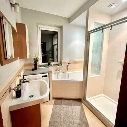 Perfect - firma sprzątająca Gdańsk Sopot Gdynia - Nowoczesna łazienka z pralką pod blatem, wanną i kabiną prysznicową, utrzymana w jasnej kolorystyce z akcentami brązu i szarości, oświetlona ciepłym światłem.