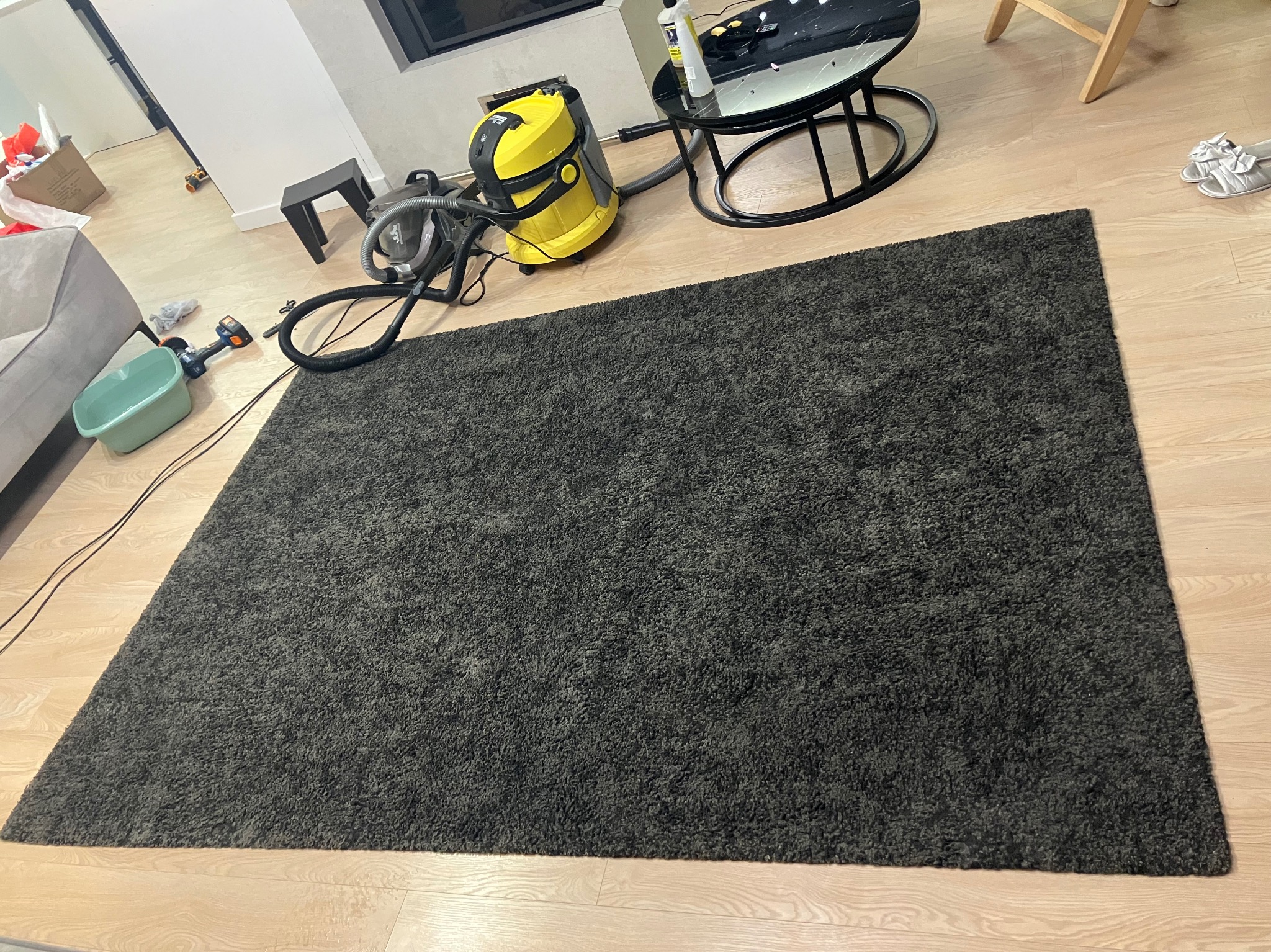 Ciemnoszary dywan z widocznym odkurzaczem piorącym Karcher w trakcie czyszczenia na jasnej drewnianej podłodze, z elementami wyposażenia wnętrza w tle.