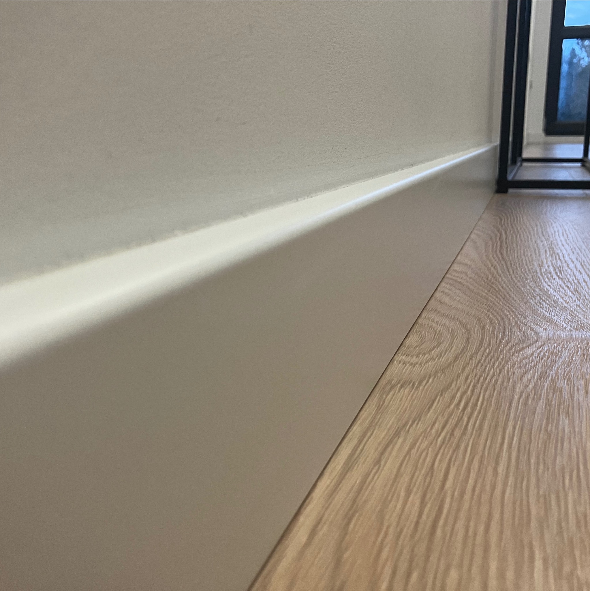 Świeżo pomalowana, biała listwa przypodłogowa na styku z panelami podłogowymi o wzorze drewna, widok z niskiej perspektywy.
