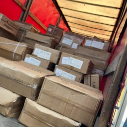 Relentless sp. z o.o. - Wnętrze ciężarówki wypełnionej kartonami z taśmą, widoczne etykiety z napisami, czerwona plandeka na dachu