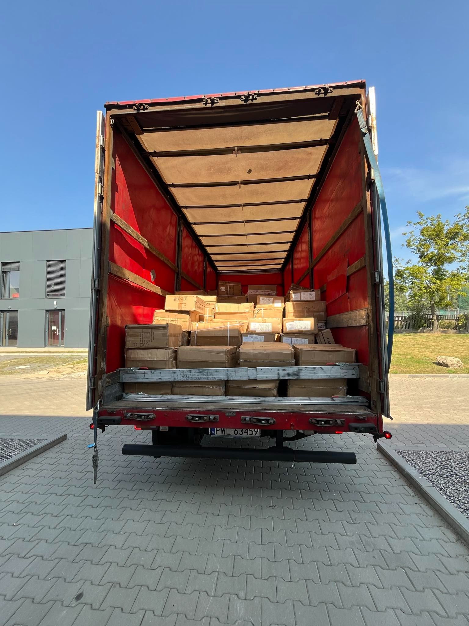 Otwarta ciężarówka wypełniona kartonami z towarem, widok z tyłu na placu załadunkowym.