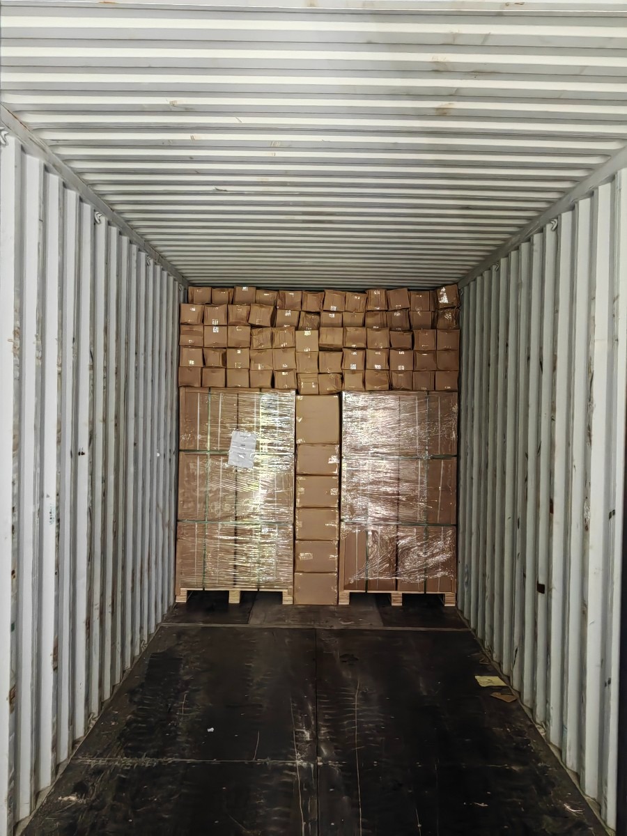 Wnętrze kontenera wypełnionego kartonami, część z nich owinięta folią stretch na paletach, widok z tyłu kontenera.