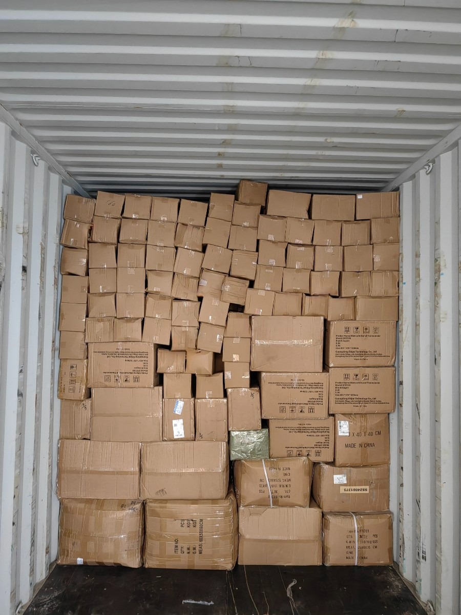 Wnętrze kontenera wypełnione kartonami różnej wielkości, niektóre owinięte folią, z widocznymi etykietami i napisami Made in China.