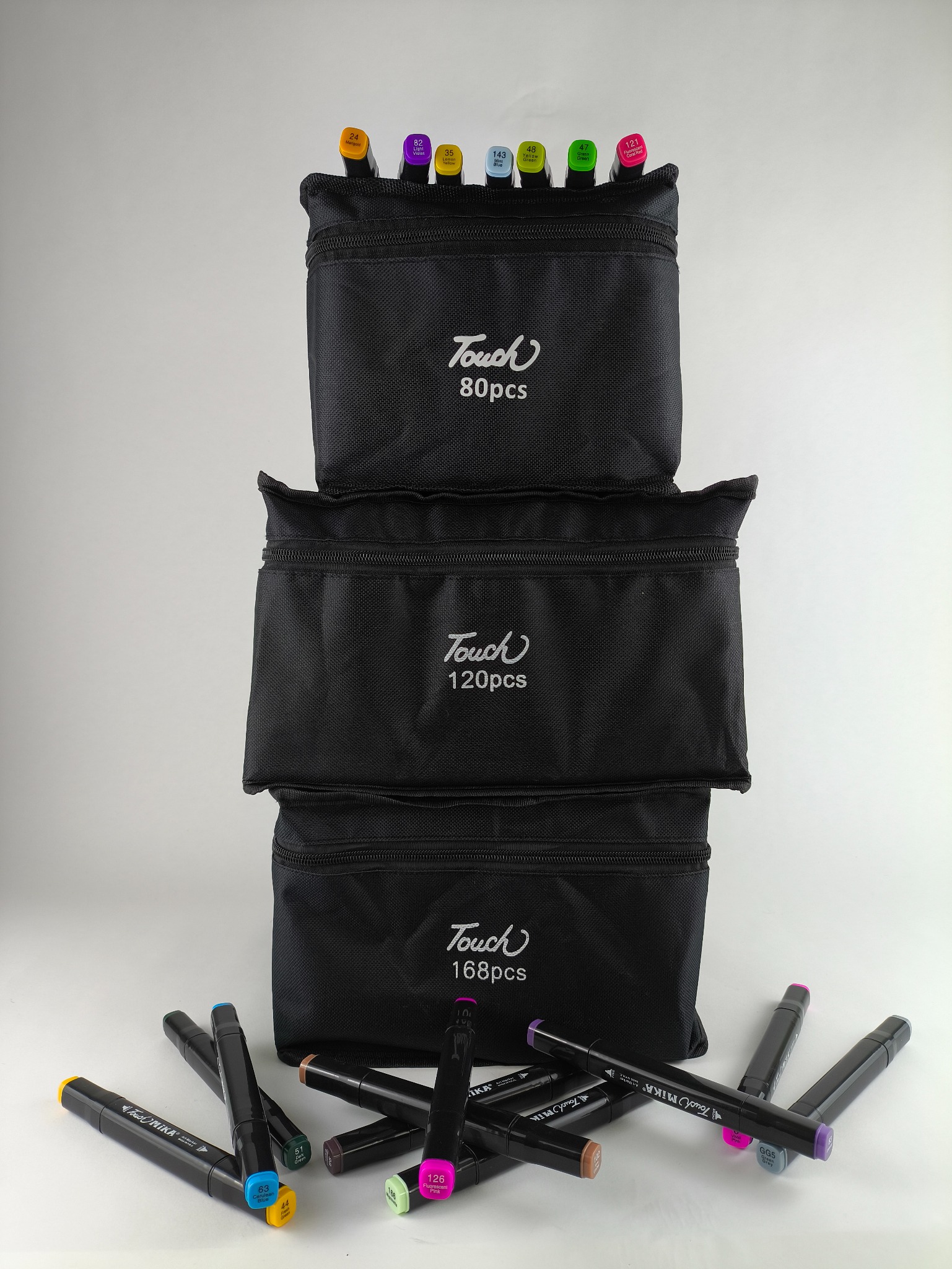 Zestaw markerów Touch Mika w trzech czarnych etui (80, 120 i 168 sztuk) ułożonych jeden na drugim, z kilkoma markerami rozłożonymi na białym tle.