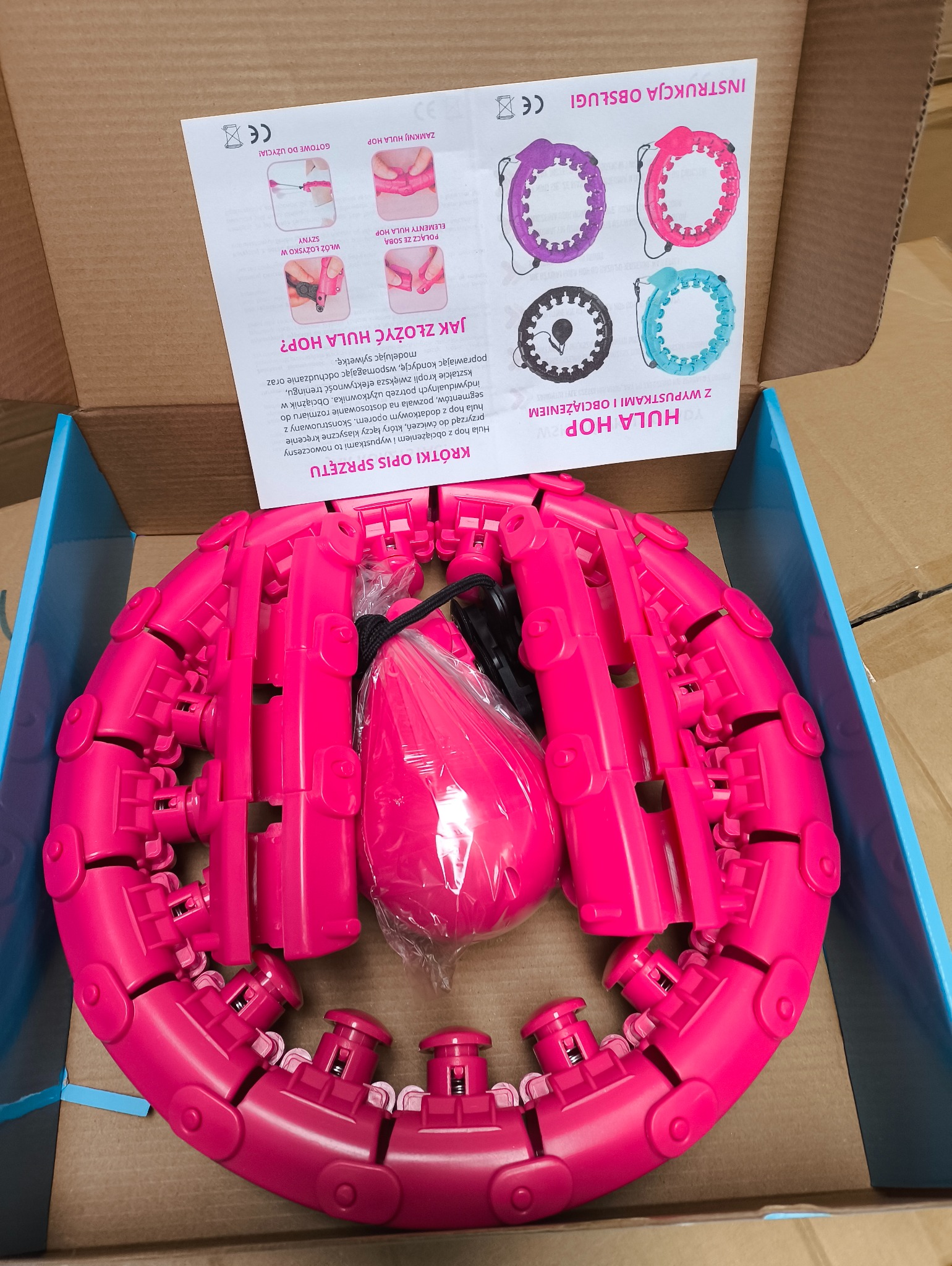 Różowe, segmentowe hula hop z obciążeniem w opakowaniu, widoczna instrukcja obsługi z objaśnieniem montażu.