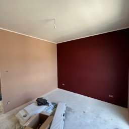 Serhii Ivanchuk - Pokój po malowaniu ścian na dwa kolory: beżowy i bordowy. Widoczne gniazdka elektryczne, narzędzia malarskie w kartonie i biała listwa przy suficie.