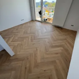 Ułożone panele w jodełkę francuską w Pruszkowie. Widok na balkon i miasto. Jasne panele, białe ściany, minimalistyczny styl wykończenia.