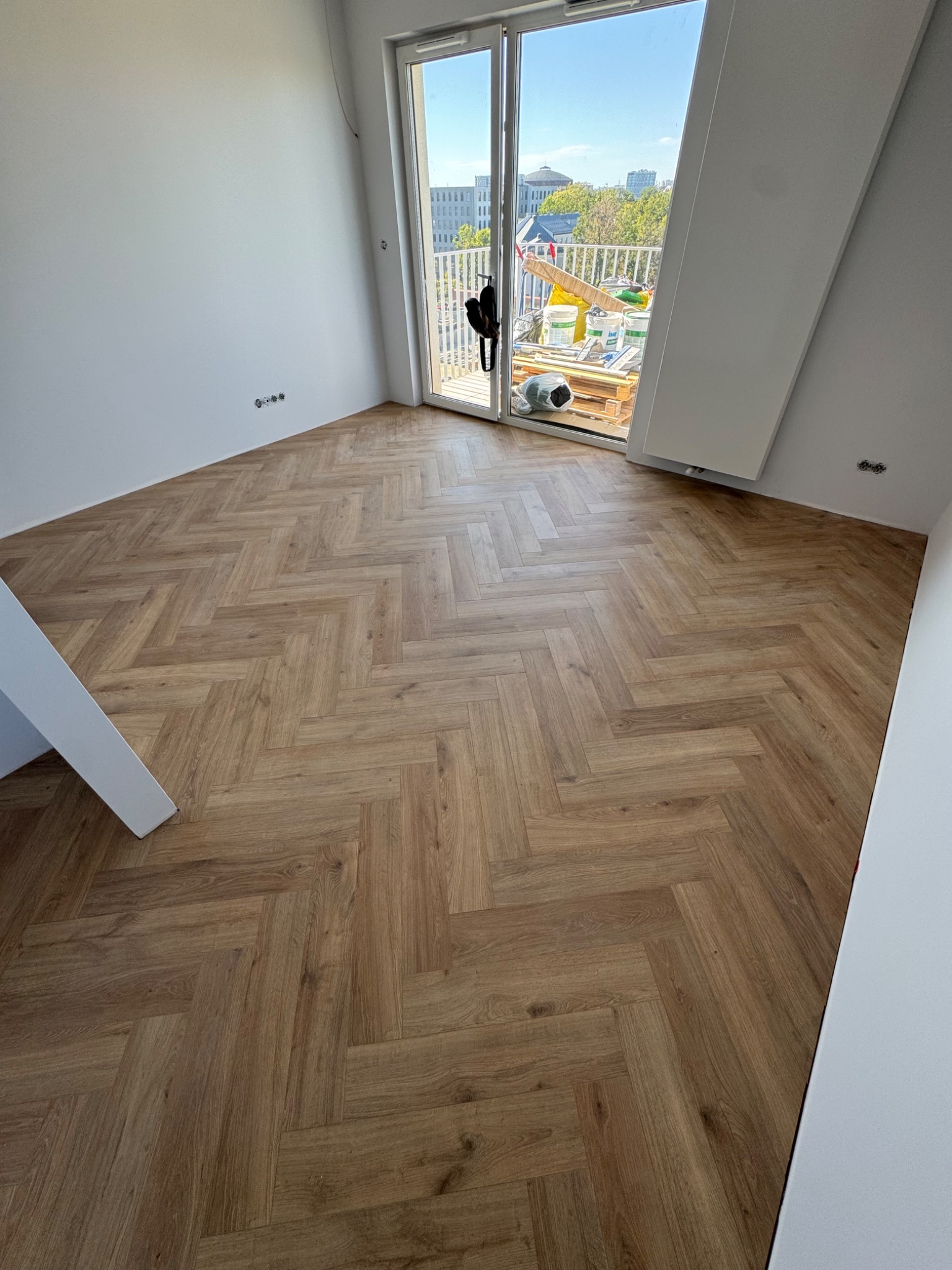 Ułożone panele w jodełkę francuską w Pruszkowie. Widok na balkon i miasto. Jasne panele, białe ściany, minimalistyczny styl wykończenia.