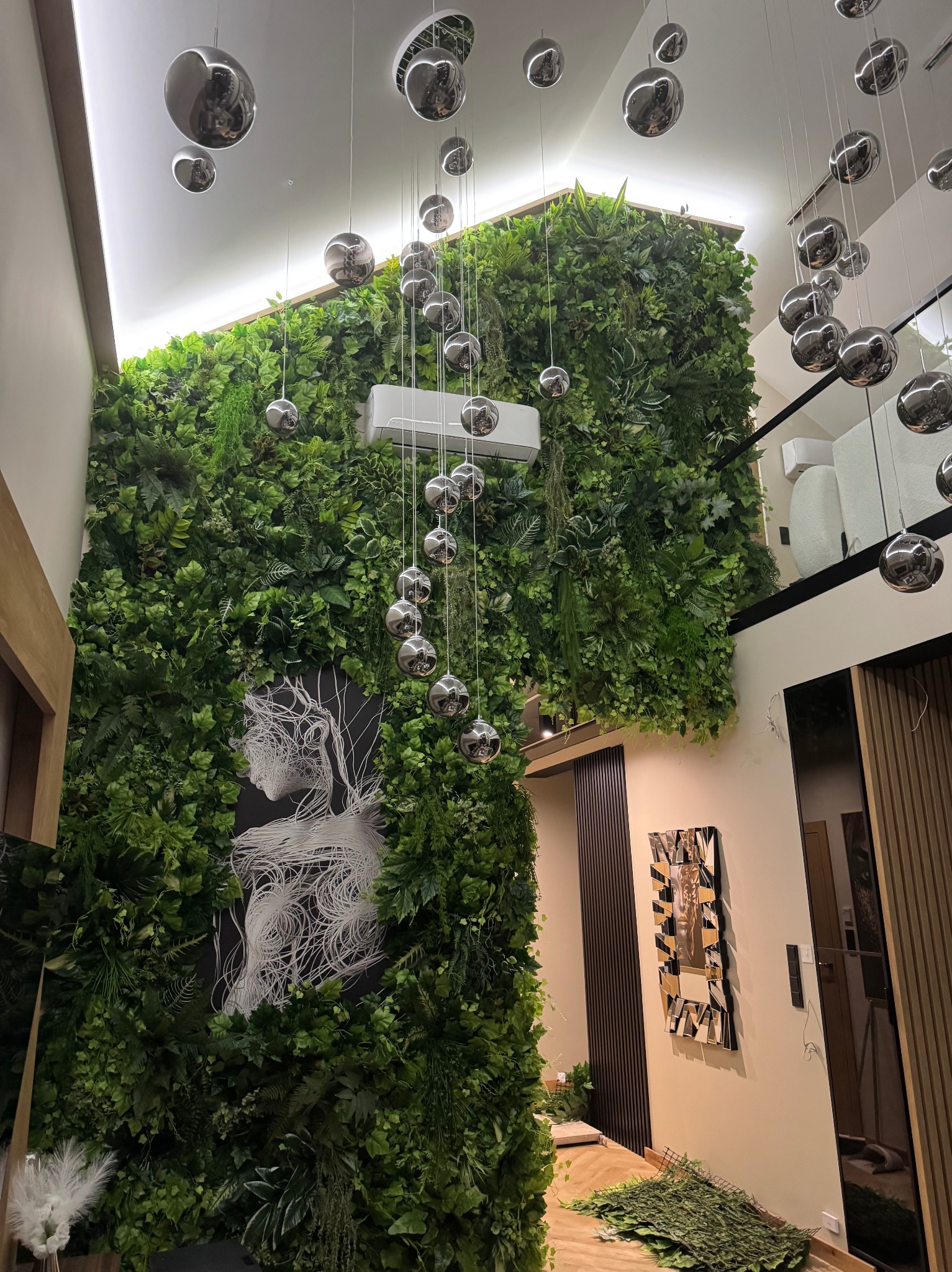 Wnętrze z zieloną ścianą, klimatyzacją i wiszącymi, srebrnymi kulami. Dekoracja uzupełniona o abstrakcyjny obraz i lustrzane elementy. Unikalny design.