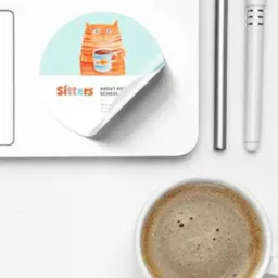 Naklejka z rysunkiem kota pijącego kawę na laptopie obok filiżanki kawy i długopisu.