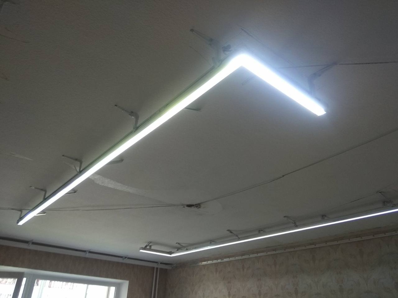 Montaż liniowych lamp LED pod sufitem z widocznymi wspornikami mocującymi i okablowaniem.