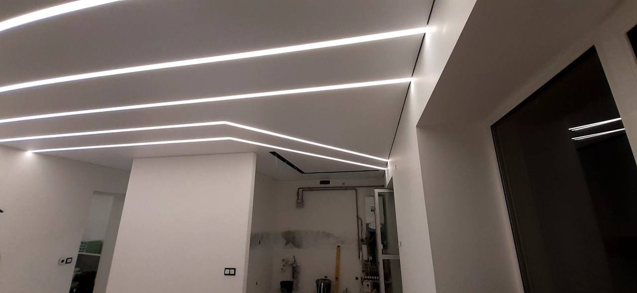 Biały sufit z wbudowanymi, liniowymi lampami LED, tworzącymi nowoczesny wzór w pomieszczeniu z białymi ścianami w trakcie remontu.