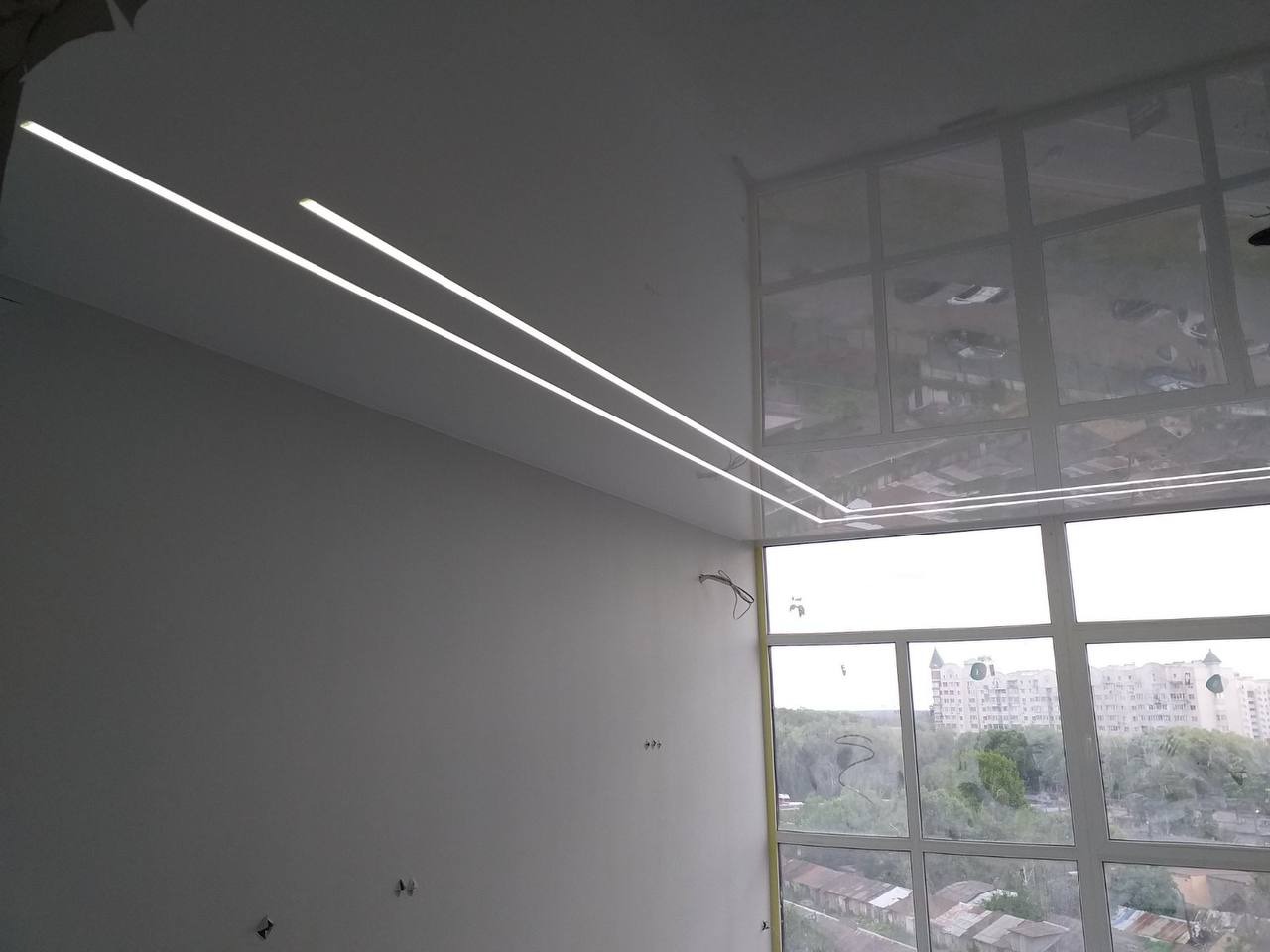 Biały, błyszczący sufit z dwiema liniami oświetlenia LED, widok na miasto przez duże okno.