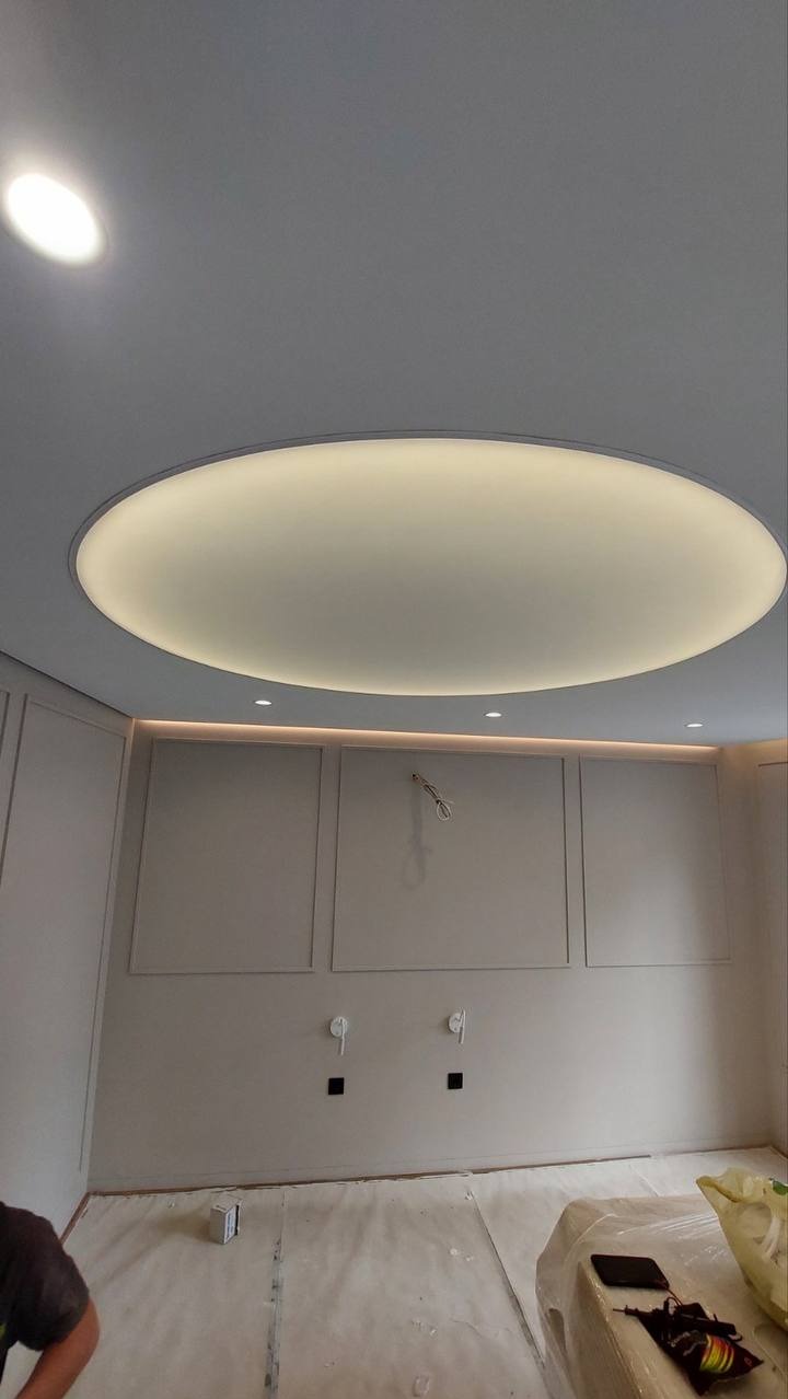 Okrągły, podświetlany element na suficie z ukrytymi punktami świetlnymi, ściana z panelami i instalacją elektryczną w trakcie montażu.