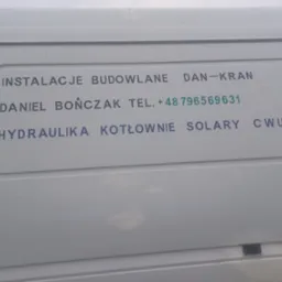 Biały samochód dostawczy z nadrukiem reklamowym: Instalacje Budowlane Dan-Kran, Daniel Bończak, numer telefonu, Hydraulika, Kotłownie, Solary, CWU.