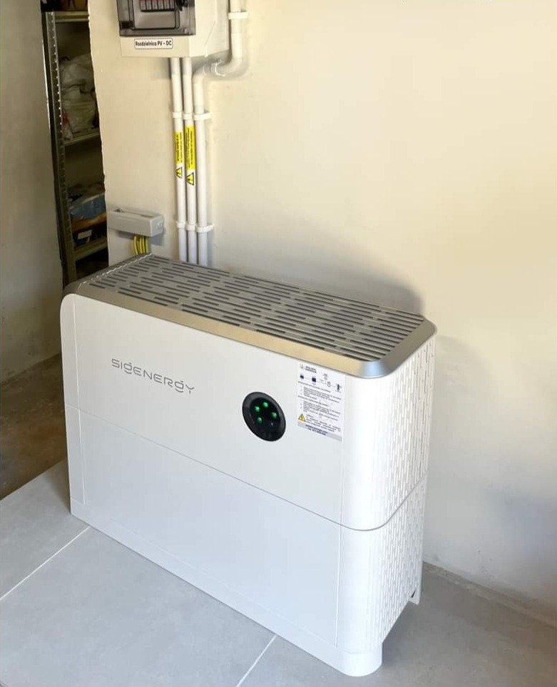 Biały magazyn energii SiCenergy w minimalistycznym wnętrzu, widoczne przewody elektryczne i rozdzielnica PV-DC na ścianie.