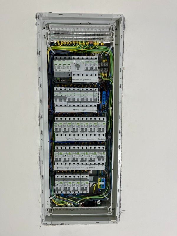 Rozdzielnica elektryczna Hager w szarej obudowie, z widocznymi zabezpieczeniami i okablowaniem, zamontowana w ścianie podczas remontu.