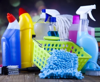 Zestaw środków czystości, w tym butelki z rozpylaczami, ściereczki z mikrofibry i mop, umieszczone w zielonym koszyku na tle ciemnego blatu. Usługi porządkowe we Wrocławiu.