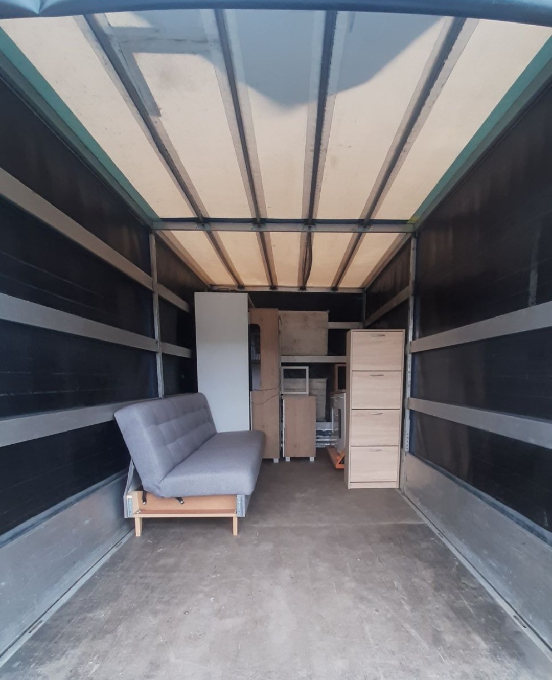 Wnętrze skrzyni ładunkowej samochodu dostawczego wypełnione meblami: rozkładana sofa, szafki i regały, przygotowane do transportu.