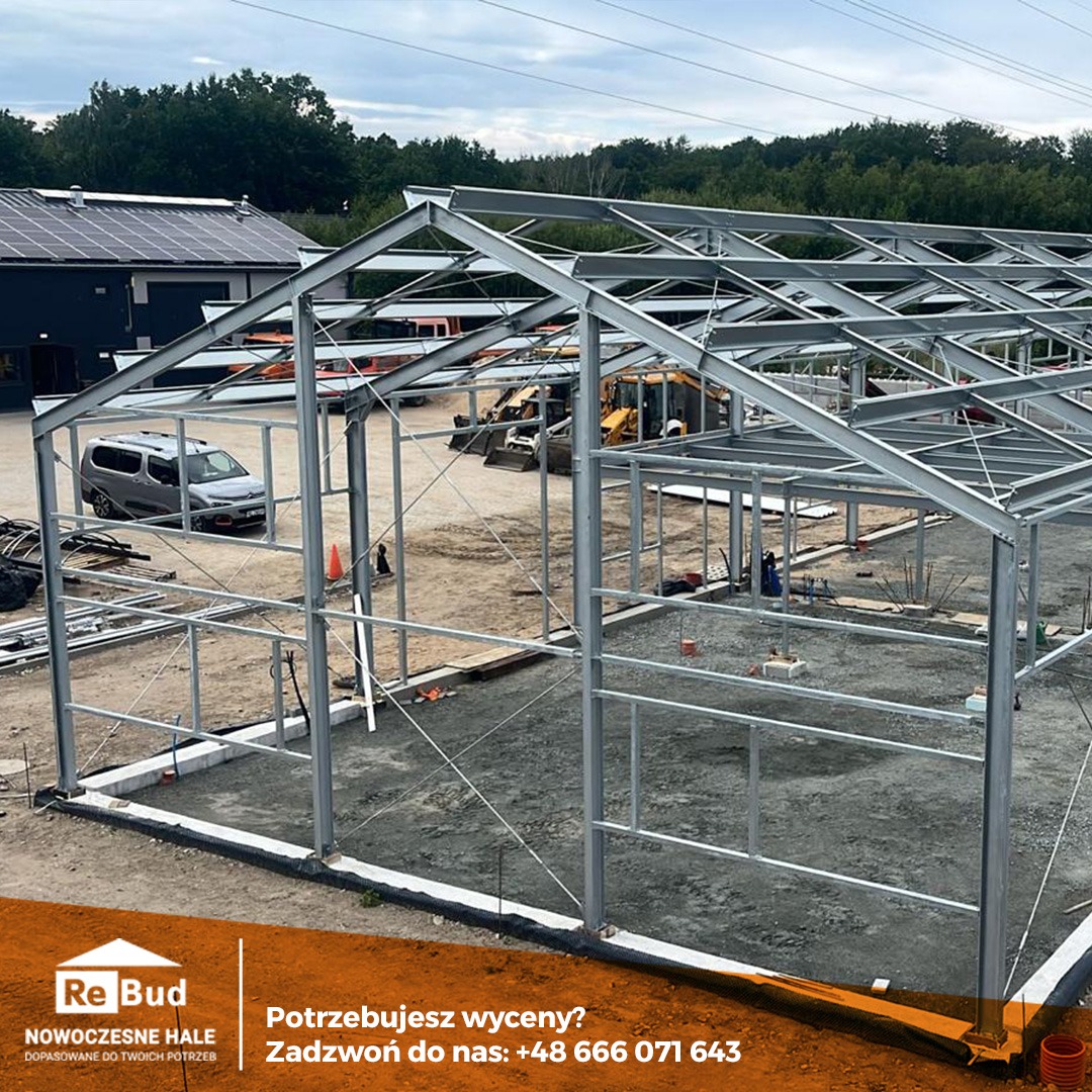 Konstrukcja stalowa hali w trakcie budowy, widoczne fundamenty, szkielet hali, maszyny budowlane w tle, budynek z panelami solarnymi w tle, boczny widok z lekkiego podwyższenia.
