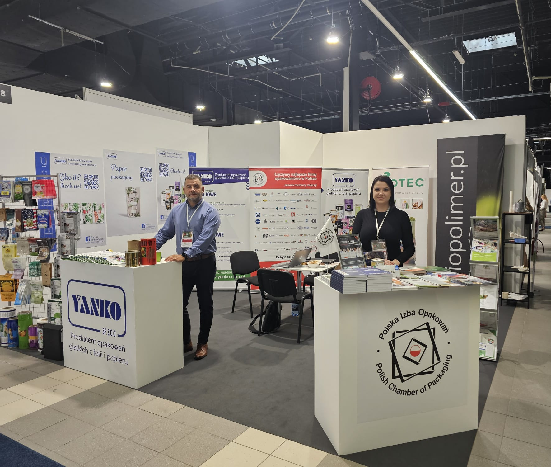 Stoisko targowe firmy Yanko prezentujące opakowania giętkie z folii i papieru, z dwoma pracownikami, materiałami reklamowymi i logo Polskiej Izby Opakowań.