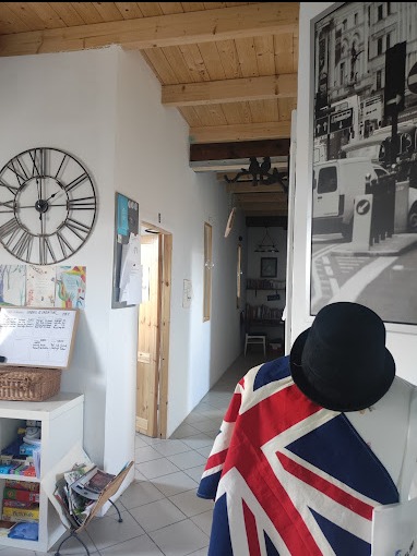 Wnętrze pokoju z elementami dekoracyjnymi w stylu brytyjskim: flaga Union Jack na manekinie, melonik, plakat z motywem Londynu, zegar ścienny w stylu vintage, biała tablica z notatkami i książki...