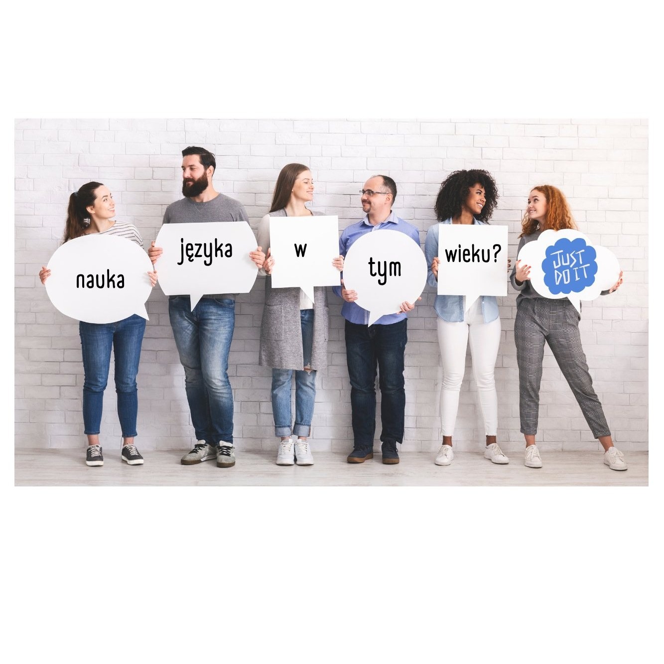 Grupa sześciu uśmiechniętych osób trzymających białe dymki z napisami: 'nauka', 'języka', 'w', 'tym', 'wieku?' i 'Just Do It' na tle białej ceglanej ściany.