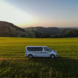 Srebrny bus na tle zielonego pola i pagórkowatego krajobrazu o zachodzie słońca, widok z lotu ptaka.